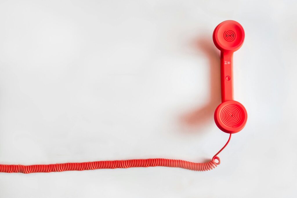 Vintage red phone handset with coiled cable on a clean white background, classic communication device.